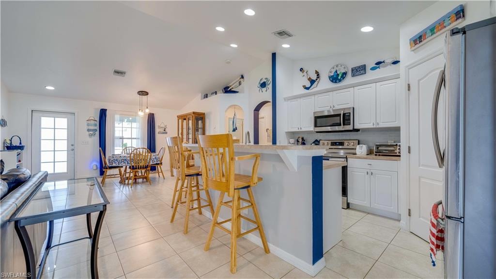 Kitchen with appliances with stainless steel finishes, white cabinetry, light countertops, a kitchen breakfast bar, and recessed lighting