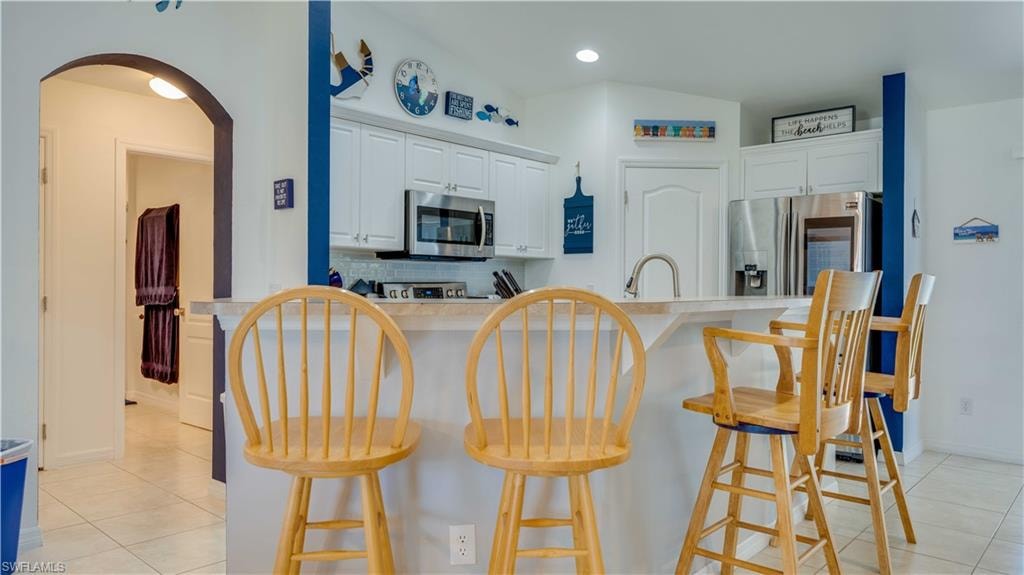 Kitchen featuring light tile patterned floors, backsplash, appliances with stainless steel finishes, arched walkways, and white cabinets