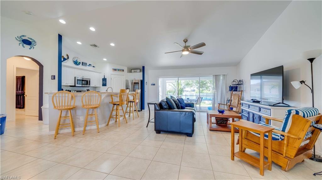 Living area featuring arched walkways, lofted ceiling, light tile patterned floors, recessed lighting, and ceiling fan