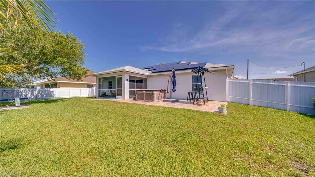Rear view of house featuring stucco siding, a fenced backyard, roof mounted solar panels, a sunroom, and a patio