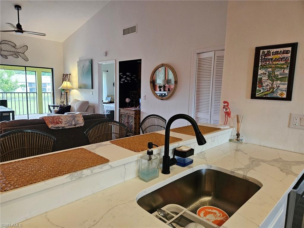 Kitchen featuring open floor plan, light stone counters, a ceiling fan, stainless steel dishwasher, and high vaulted ceiling