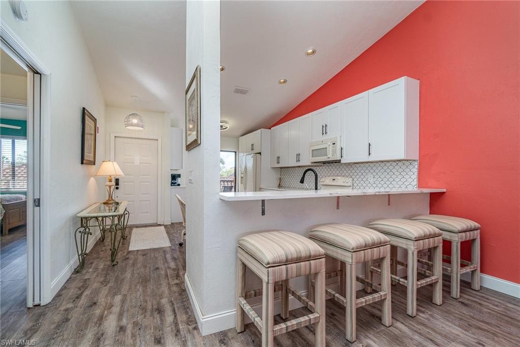 Kitchen with a breakfast bar, lofted ceiling, white cabinets, dark wood-type flooring, and decorative backsplash