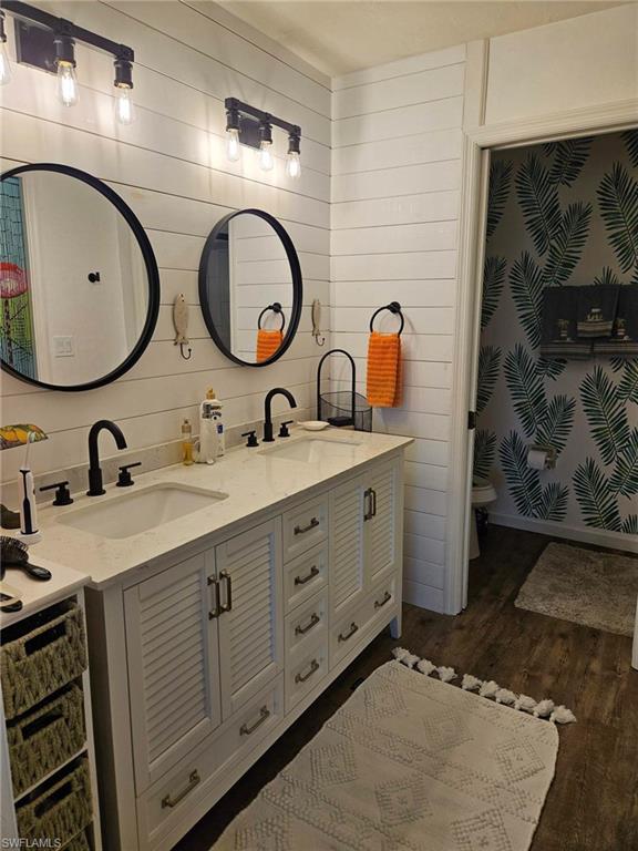 Full bath featuring double vanity, dark wood-type flooring, and wooden walls