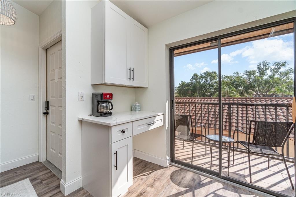 Kitchen featuring white cabinetry, light stone countertops, light wood-style flooring, and built in desk