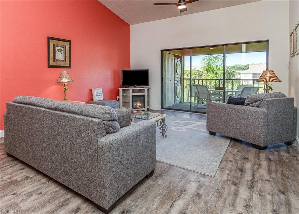 Living room featuring vaulted ceiling, wood finished floors, ceiling fan, and a warm lit fireplace