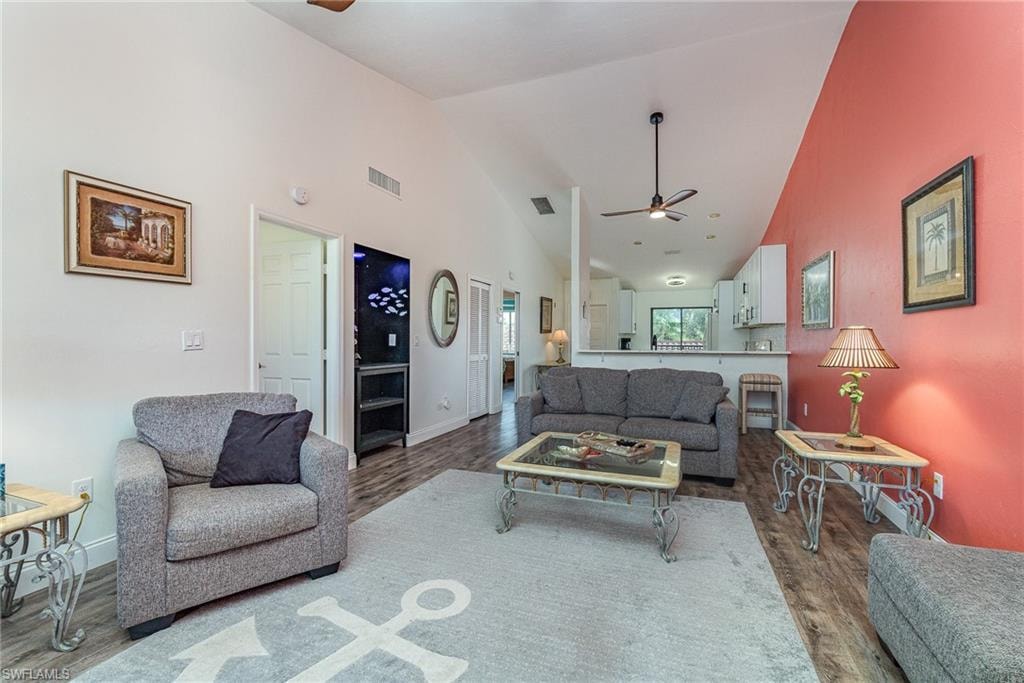 Living room featuring a ceiling fan, dark wood-type flooring, and high vaulted ceiling