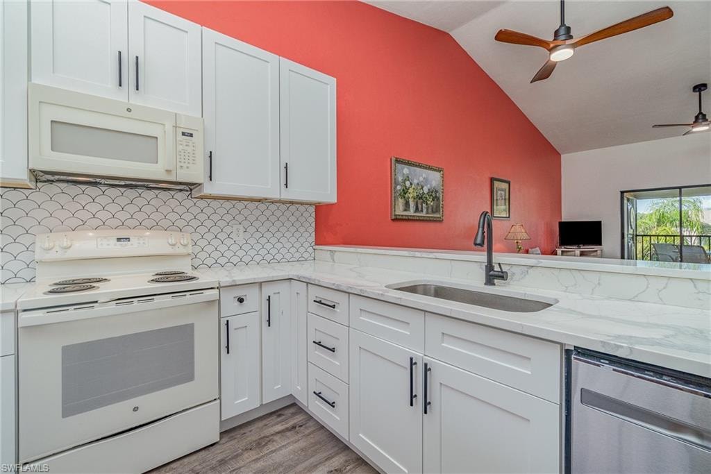 Kitchen featuring white appliances, light stone countertops, a ceiling fan, backsplash, and white cabinets