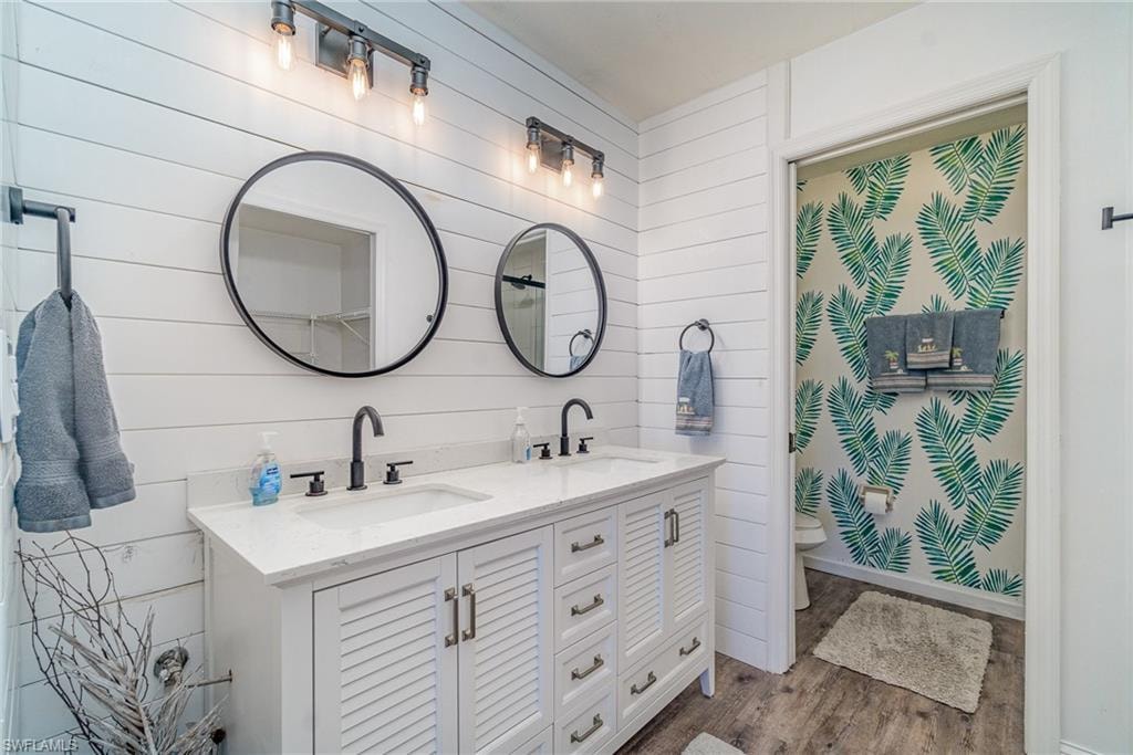 Full bathroom featuring double vanity, dark wood-type flooring, and wooden walls