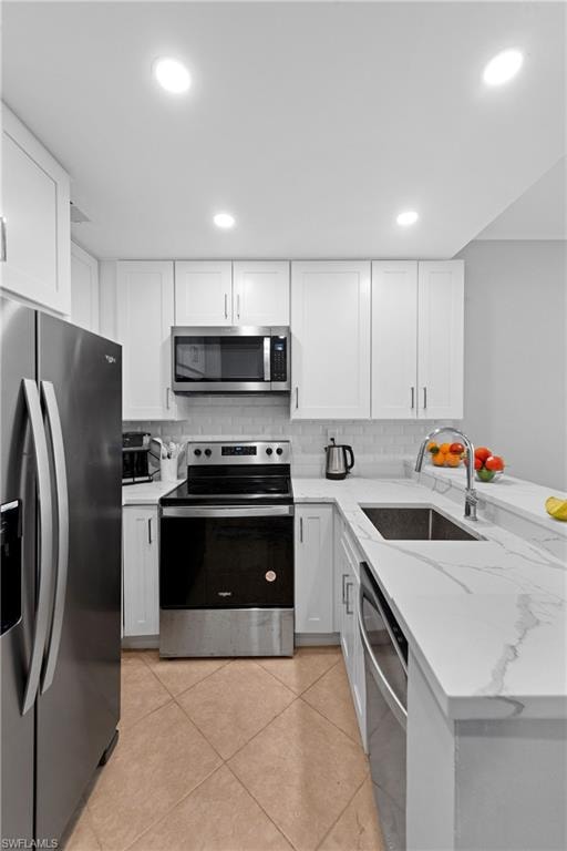 Kitchen with appliances with stainless steel finishes, light stone counters, tasteful backsplash, white cabinets, and light tile patterned flooring