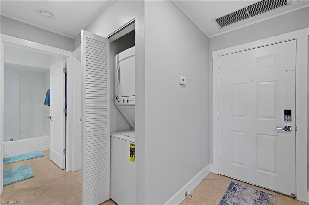 Laundry area featuring light tile patterned floors and stacked washing machine and dryer