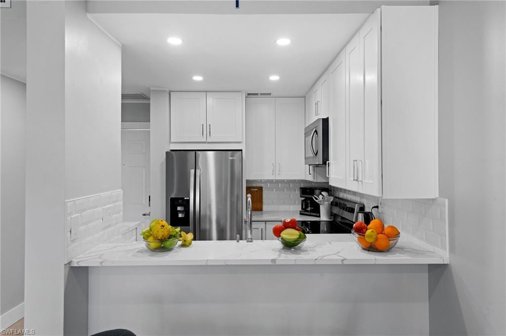 Kitchen with decorative backsplash, recessed lighting, light stone counters, appliances with stainless steel finishes, and white cabinetry