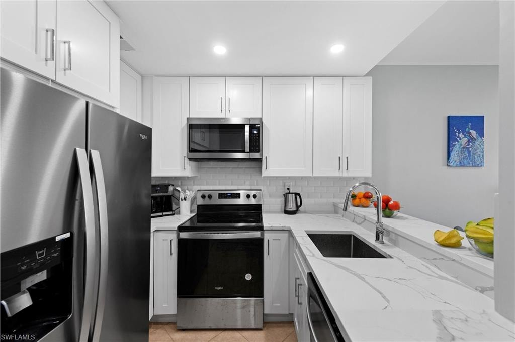 Kitchen featuring stainless steel appliances, light stone countertops, backsplash, white cabinets, and recessed lighting