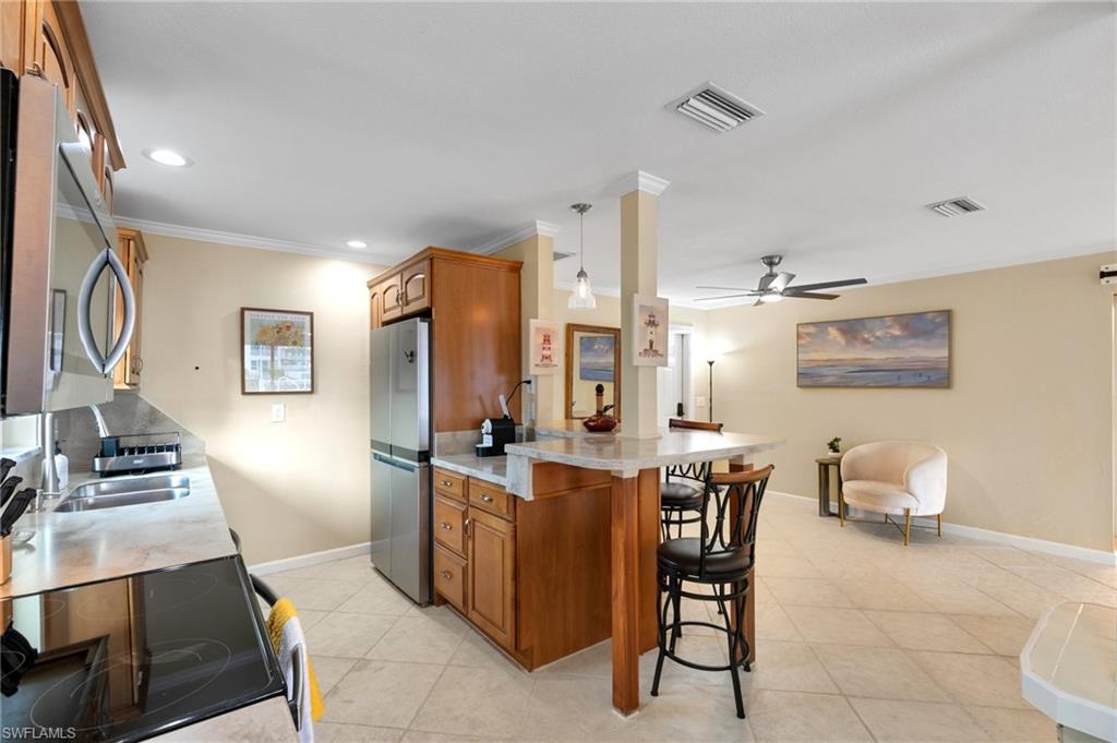 Kitchen with brown cabinets, appliances with stainless steel finishes, a kitchen bar, ornamental molding, and light tile patterned floors