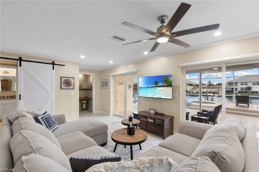 Tiled living area featuring ornamental molding, a barn door, recessed lighting, and a ceiling fan