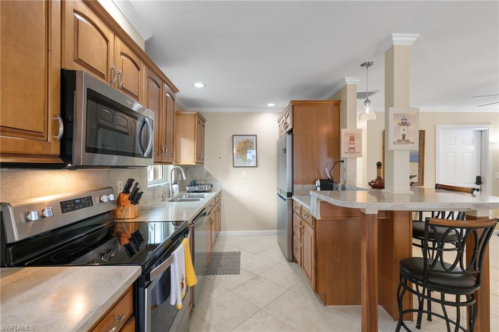 Kitchen featuring appliances with stainless steel finishes, brown cabinetry, a breakfast bar area, ornamental molding, and pendant lighting