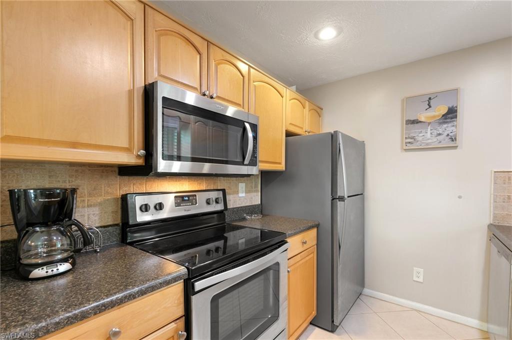 Kitchen with appliances with stainless steel finishes, backsplash, dark countertops, light tile patterned flooring, and light brown cabinetry