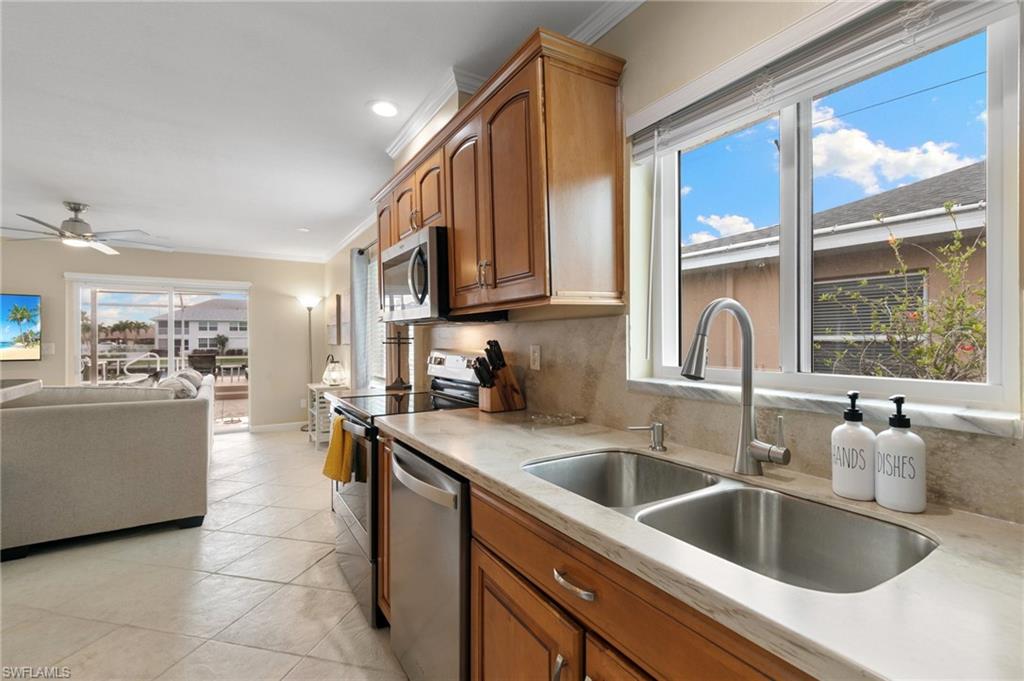 Kitchen with open floor plan, crown molding, appliances with stainless steel finishes, brown cabinetry, and light stone countertops