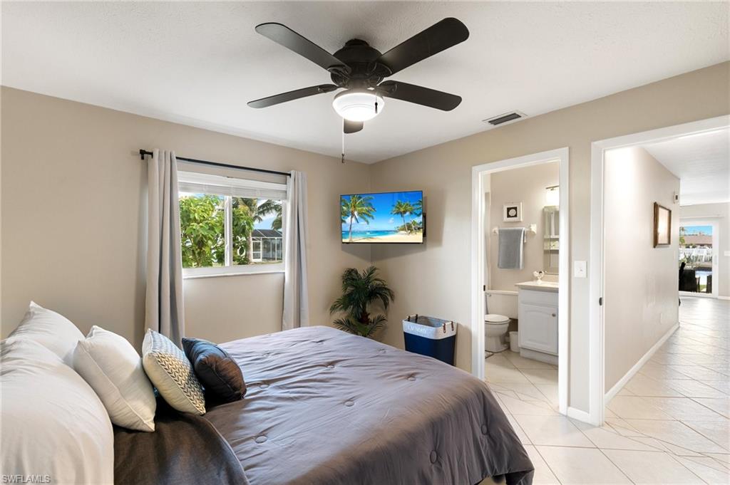 Bedroom with light tile patterned floors, ceiling fan, and ensuite bath