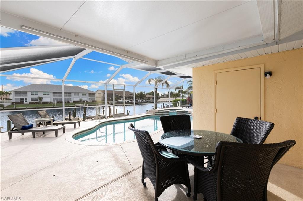 View of pool with a patio, a sunroom, a water view, glass enclosure, and a pool with connected hot tub