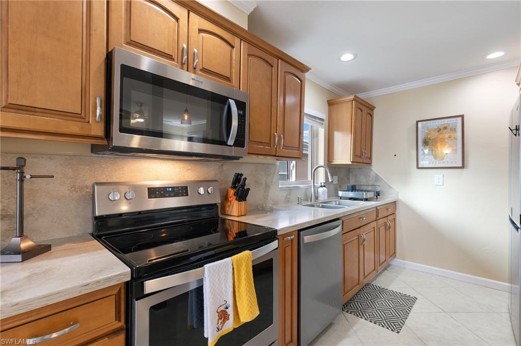 Kitchen featuring stainless steel appliances, brown cabinetry, tasteful backsplash, light stone counters, and crown molding
