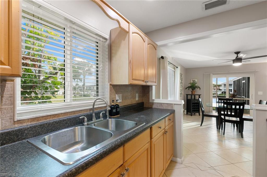 Kitchen with dark countertops, tasteful backsplash, light tile patterned floors, ceiling fan, and light brown cabinets