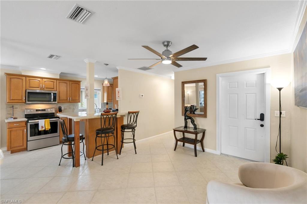 Kitchen featuring appliances with stainless steel finishes, a breakfast bar area, light countertops, ornamental molding, and a ceiling fan