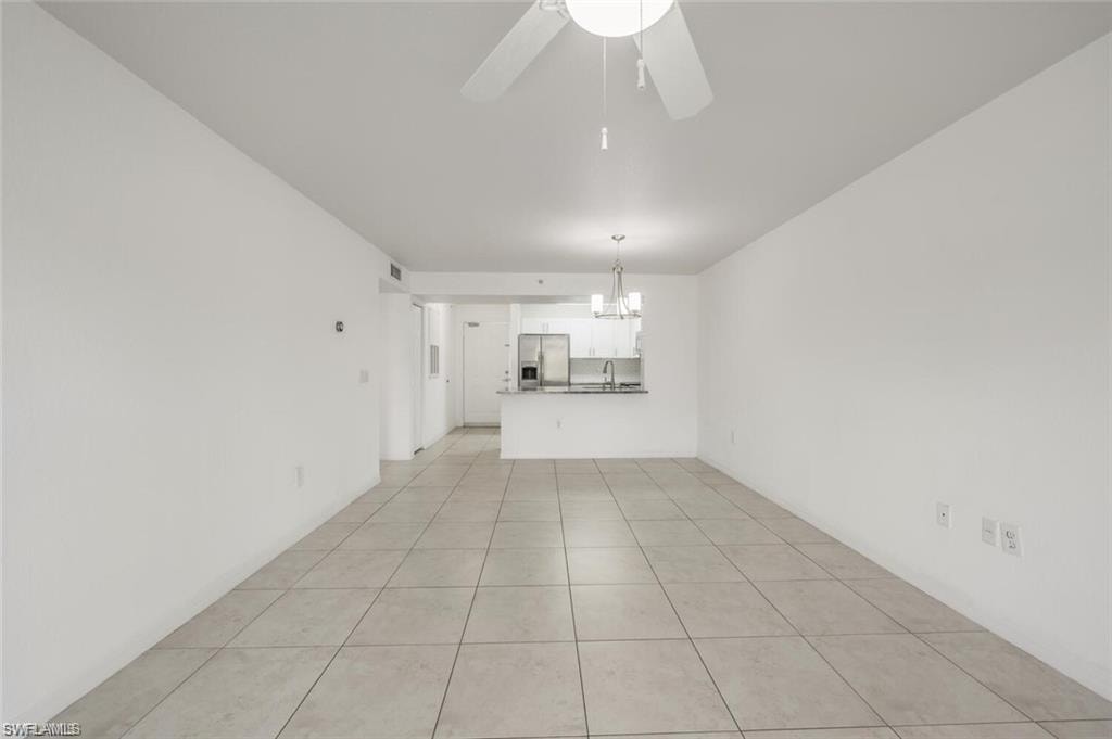 Unfurnished living room featuring light tile patterned flooring, a ceiling fan, and a chandelier