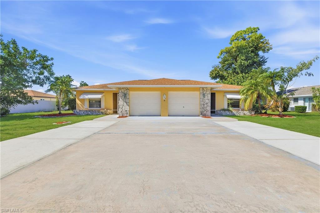 Duplex featuring stone siding, a front yard, and stucco siding, concrete drive way and a yard.