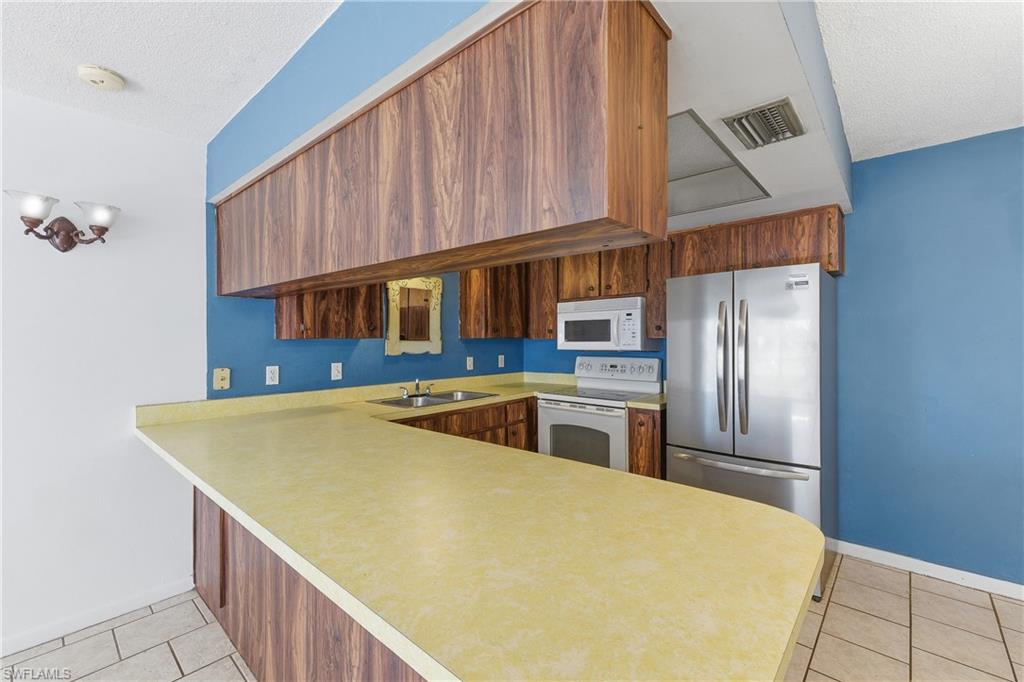 Kitchen with light countertops, a peninsula, white appliances, a textured ceiling, and light tile patterned floors