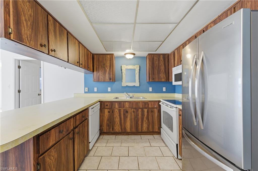 Kitchen with white appliances, light countertops, light tile patterned flooring, and wood finish cabinets