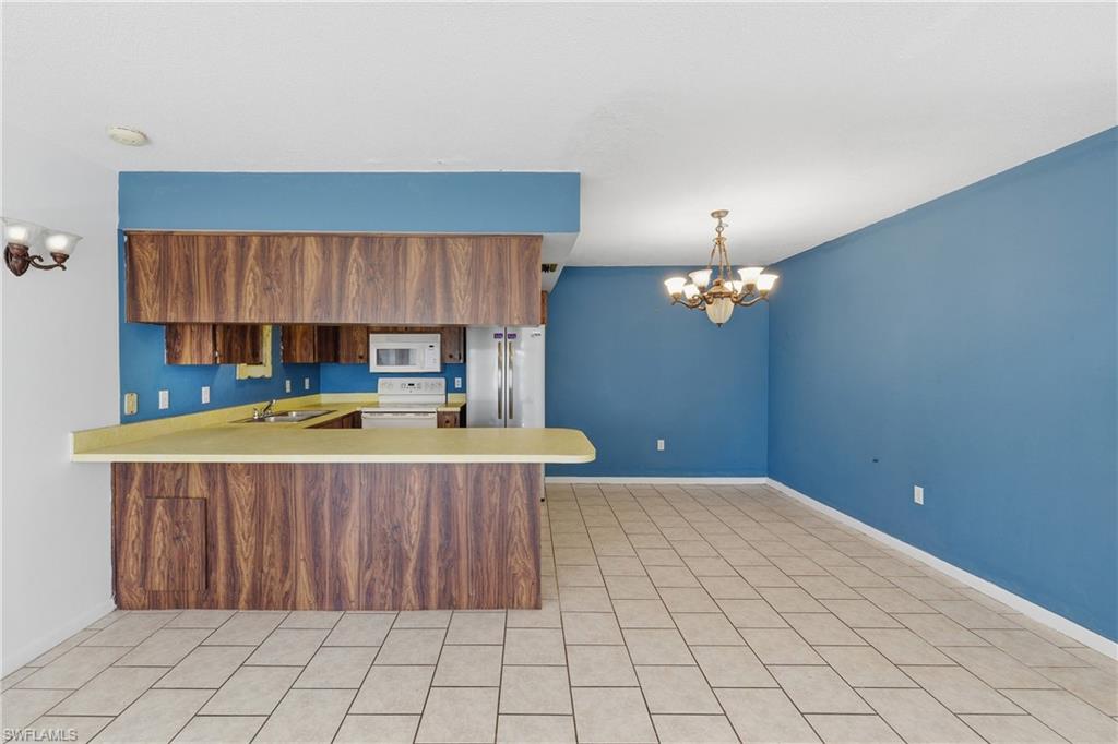 Kitchen featuring a chandelier, light countertops, a peninsula, wood finish cabinets, and white appliances
