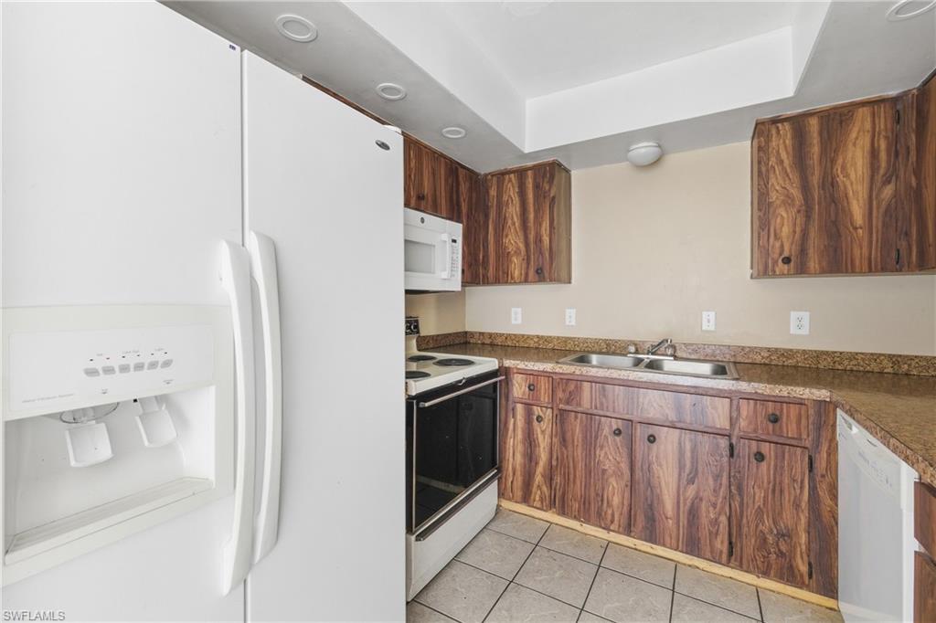 Kitchen featuring white appliances, light tile patterned floors, dark countertops, and a tray ceiling