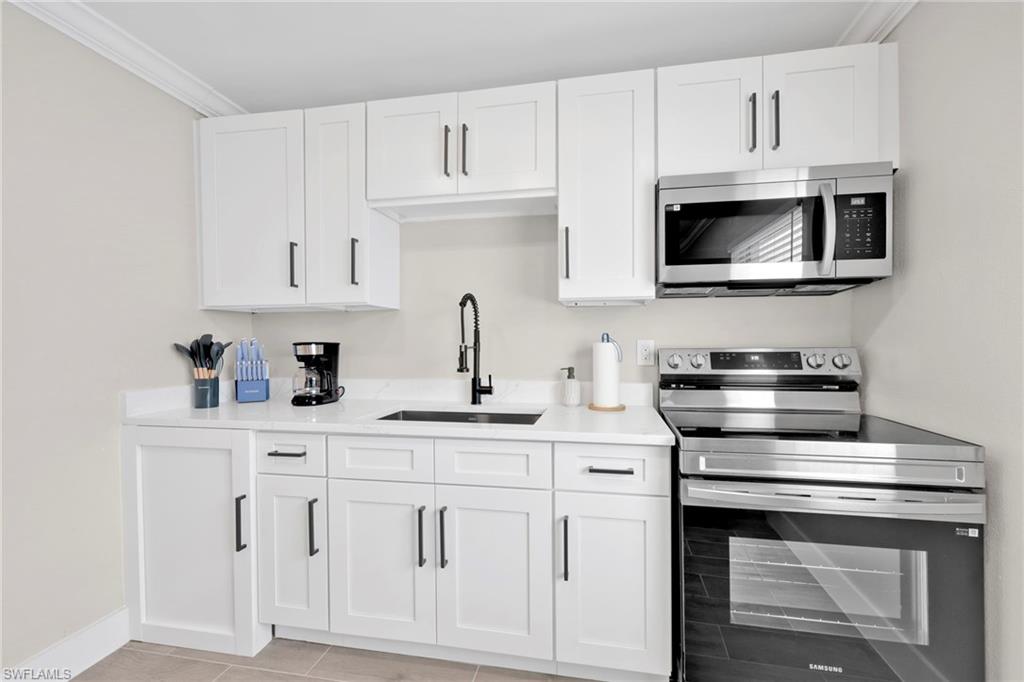 Kitchen with appliances with stainless steel finishes, white cabinets, light stone countertops, and crown molding