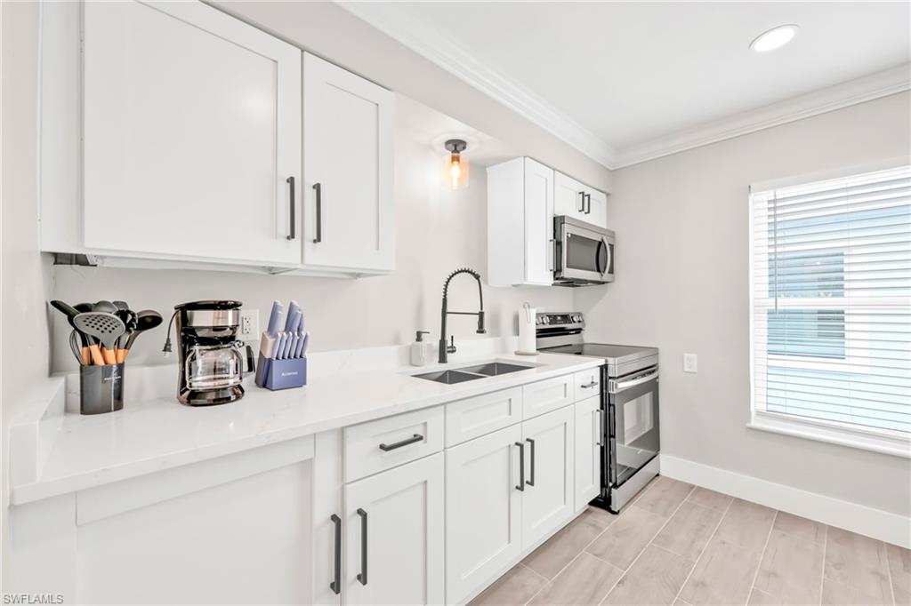Kitchen with ornamental molding, stainless steel appliances, white cabinets, light stone counters, and wood finish floors