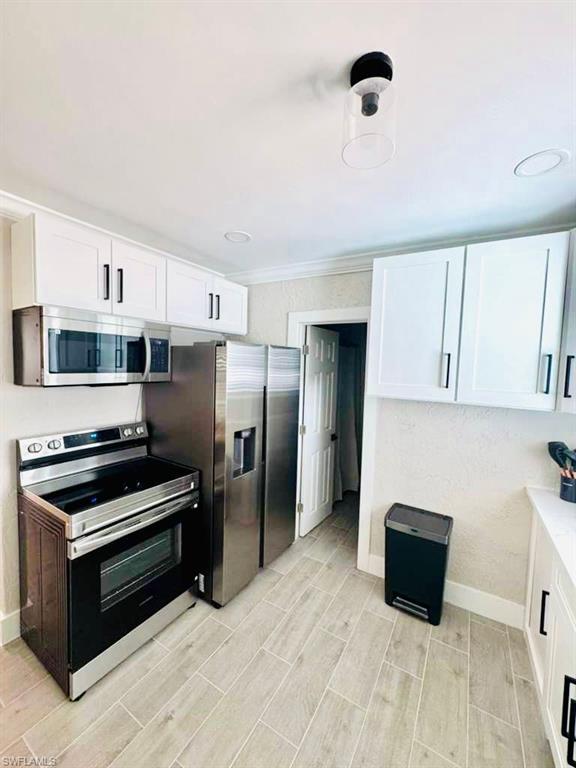 Kitchen featuring appliances with stainless steel finishes, white cabinets, wood tiled floors, crown molding, and light stone counters