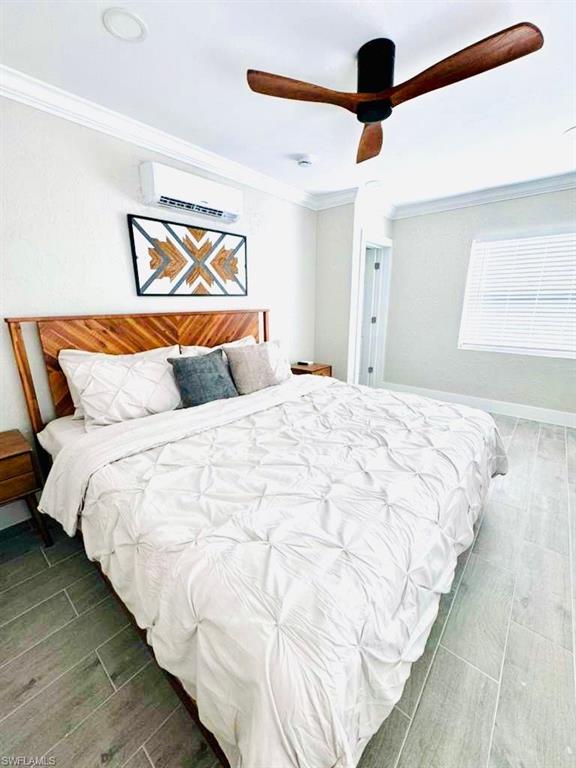 Bedroom featuring wood tiled floors, ornamental molding, a ceiling fan, and an AC wall unit