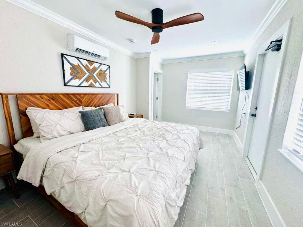 Bedroom featuring ornamental molding, wood tiled floors, a ceiling fan, and a wall unit AC