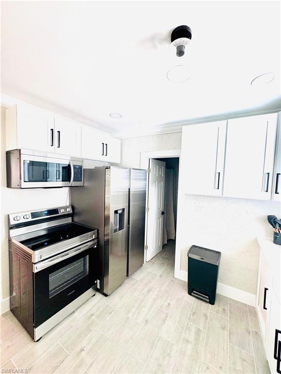 Kitchen featuring stainless steel appliances, white cabinetry, wood finish floors, and crown molding