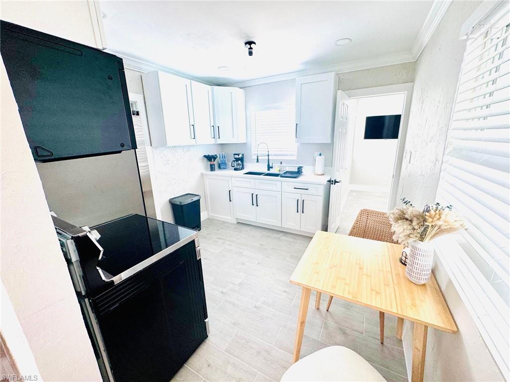 Kitchen with white cabinetry, black electric range oven, light countertops, crown molding, and light wood-type flooring