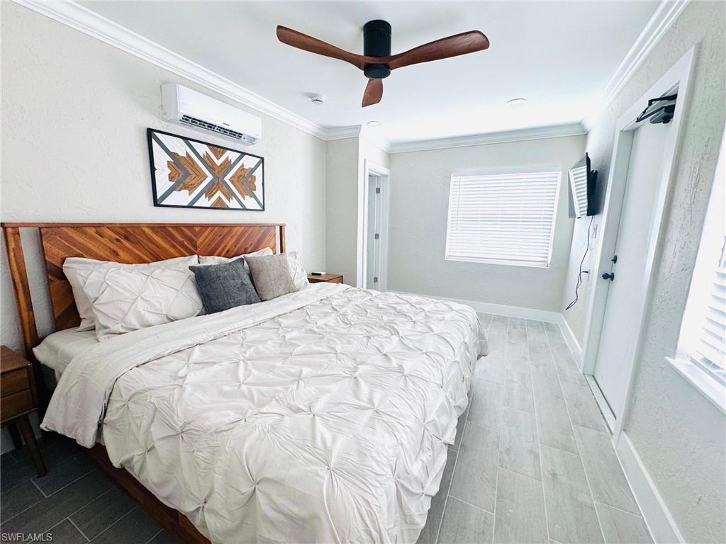 Bedroom with crown molding, wood finish floors, a textured wall, a ceiling fan, and a wall mounted AC
