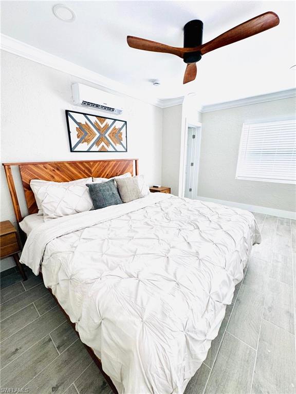 Bedroom featuring wood tiled floors, ornamental molding, ceiling fan, and an AC wall unit