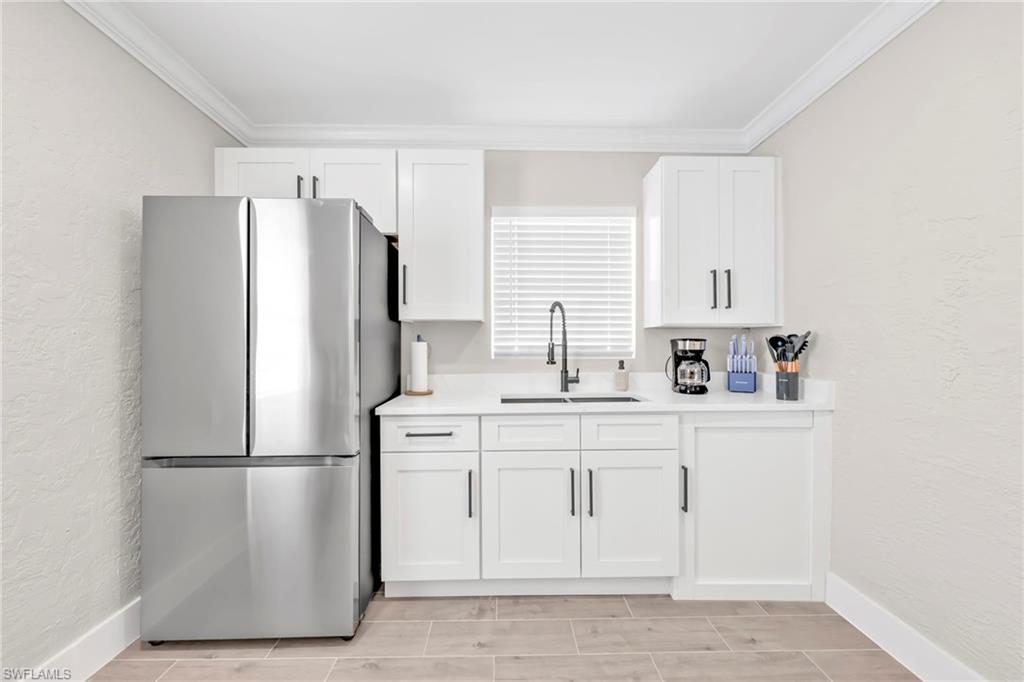 Kitchen with a textured wall, freestanding refrigerator, ornamental molding, white cabinetry, and wood tiled floors