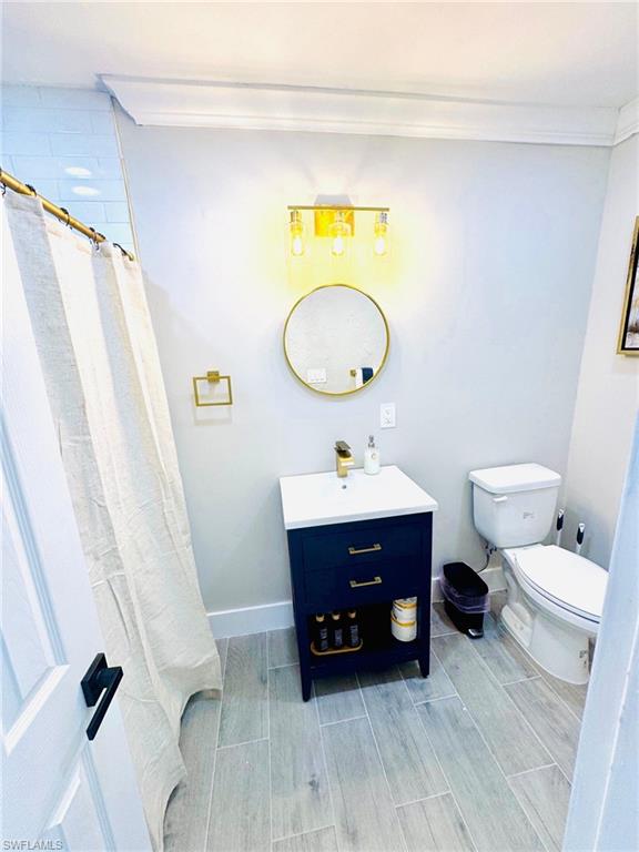 Full bathroom with a shower with shower curtain, wood tiled floors, vanity, and ornamental molding