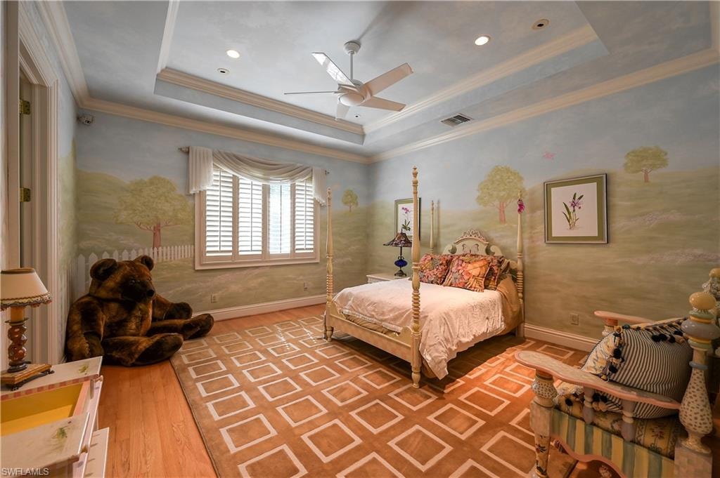 Bedroom with a tray ceiling, ornamental molding, light wood finished floors, and a ceiling fan