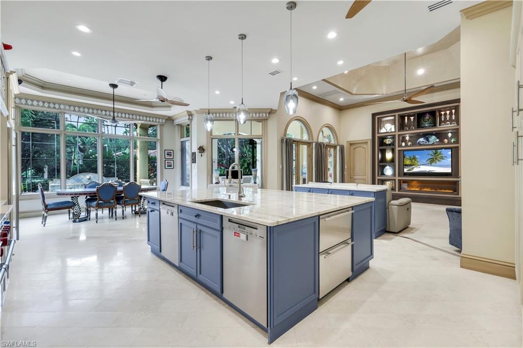 Kitchen with blue cabinetry, a tray ceiling, ceiling fan, crown molding, and light stone counters