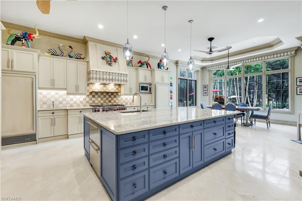 Kitchen with a ceiling fan, hanging light fixtures, ornamental molding, light stone counters, and a raised ceiling