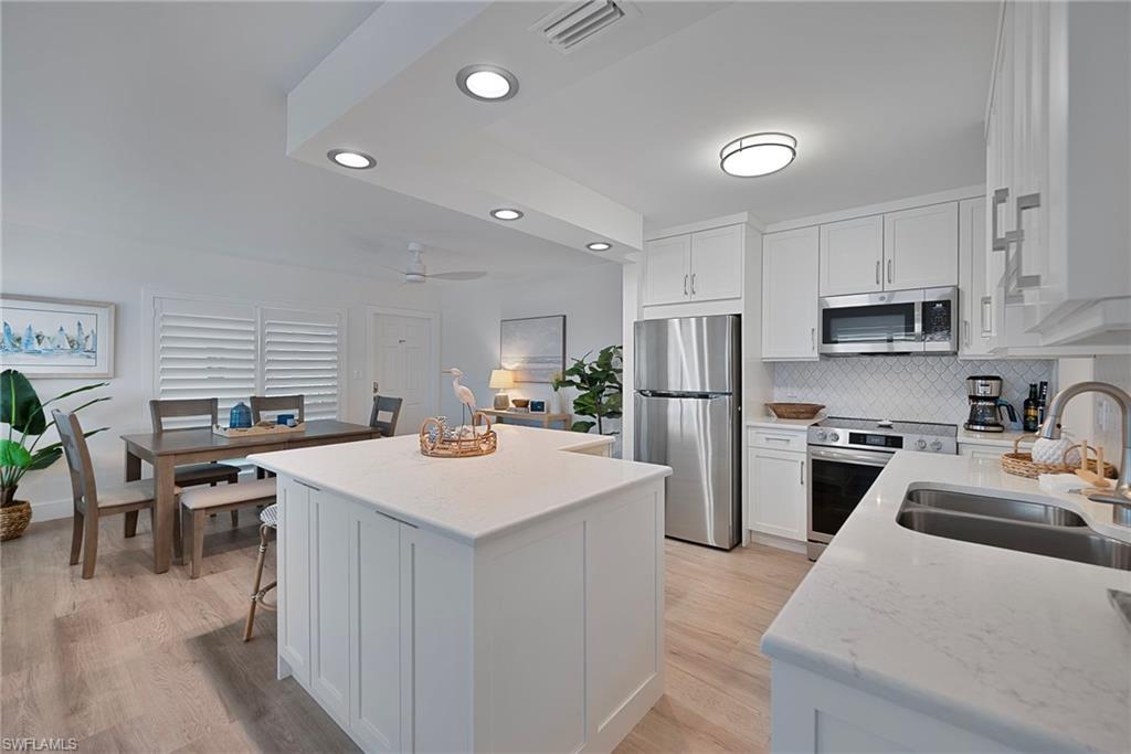 Kitchen featuring recessed lighting, white cabinetry, decorative backsplash, stainless steel appliances, and a kitchen island