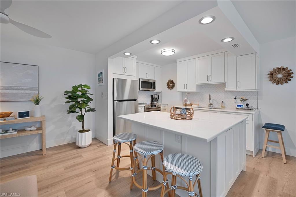 Kitchen with white cabinets, decorative backsplash, light wood-type flooring, stainless steel appliances, and recessed lighting