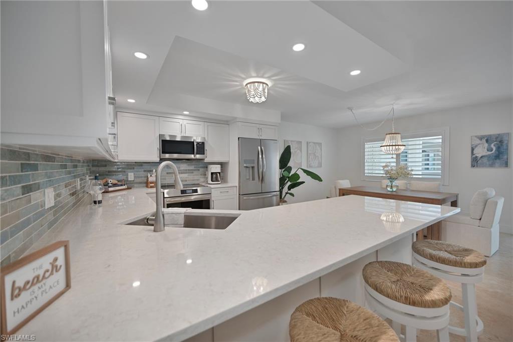 Kitchen with a peninsula, backsplash, white cabinetry, light stone counters, and stainless steel appliances