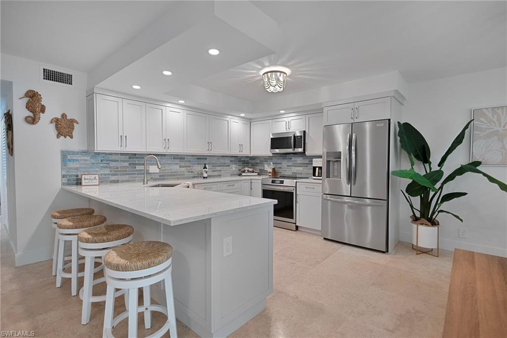 Kitchen featuring stainless steel appliances, a peninsula, tasteful backsplash, a kitchen breakfast bar, and light stone countertops